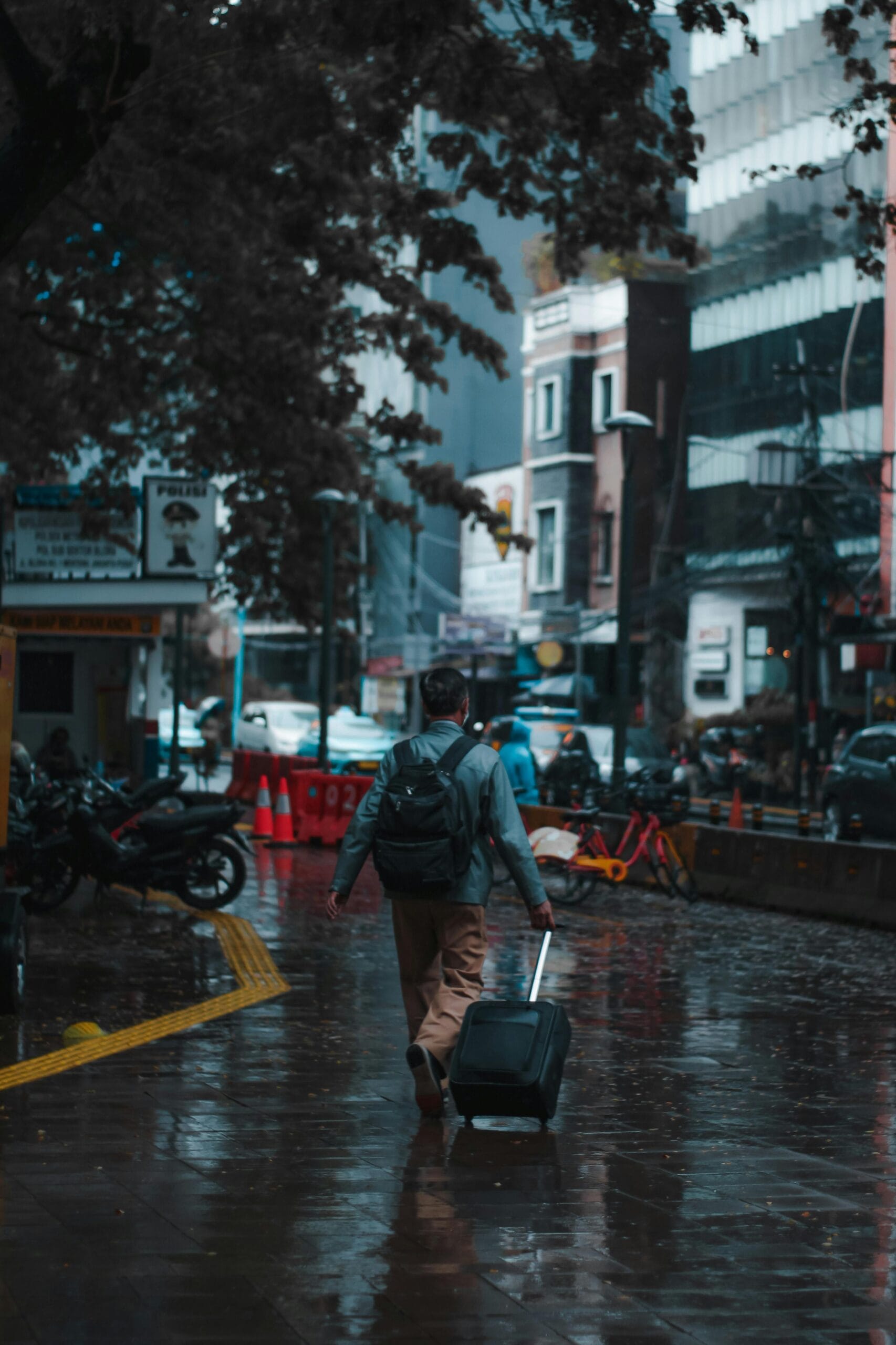 A man with a backpack pulls luggage on a wet city street in Jakarta, Indonesia.
